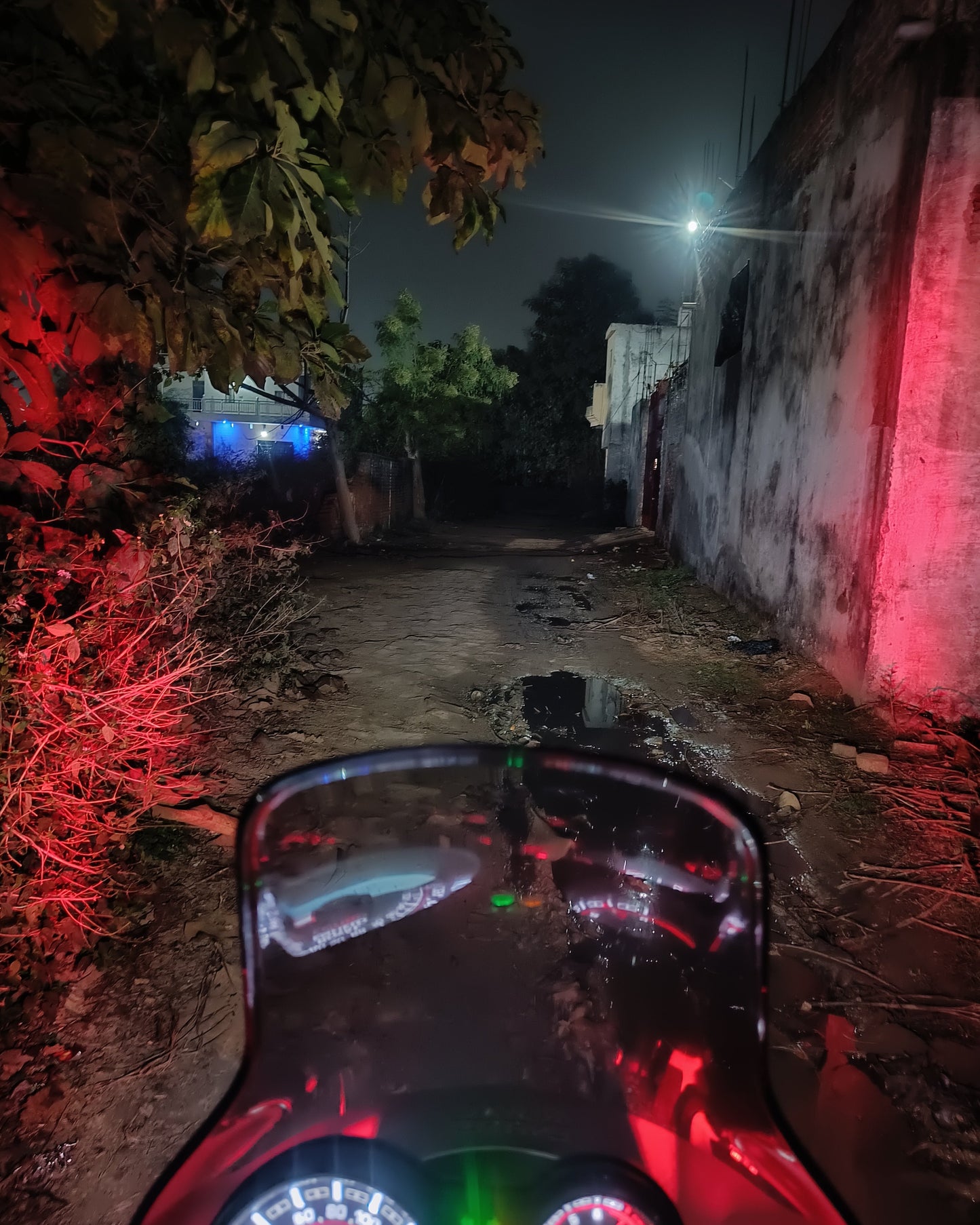 Motorcycle dashboard view at night with red lights on a dark street.