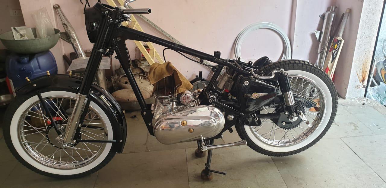 A black motorcycle with white wall inserts on the tires, displayed indoors, indicating a classic vintage style.