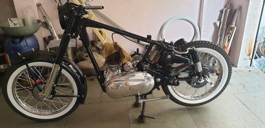 A black motorcycle with white wall inserts on the tires, displayed indoors, indicating a classic vintage style.