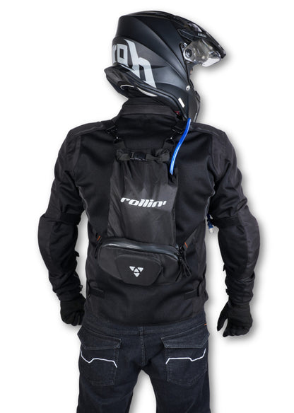 Shift-Pack_06.jpg: Rear view of a helmeted rider wearing the Rollin’Denims Shift-Pack backpack with a blue hydration tube, at MotoARZT.