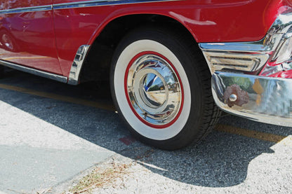 Close-up of a red classic car's wheel with white wall tire on a road.